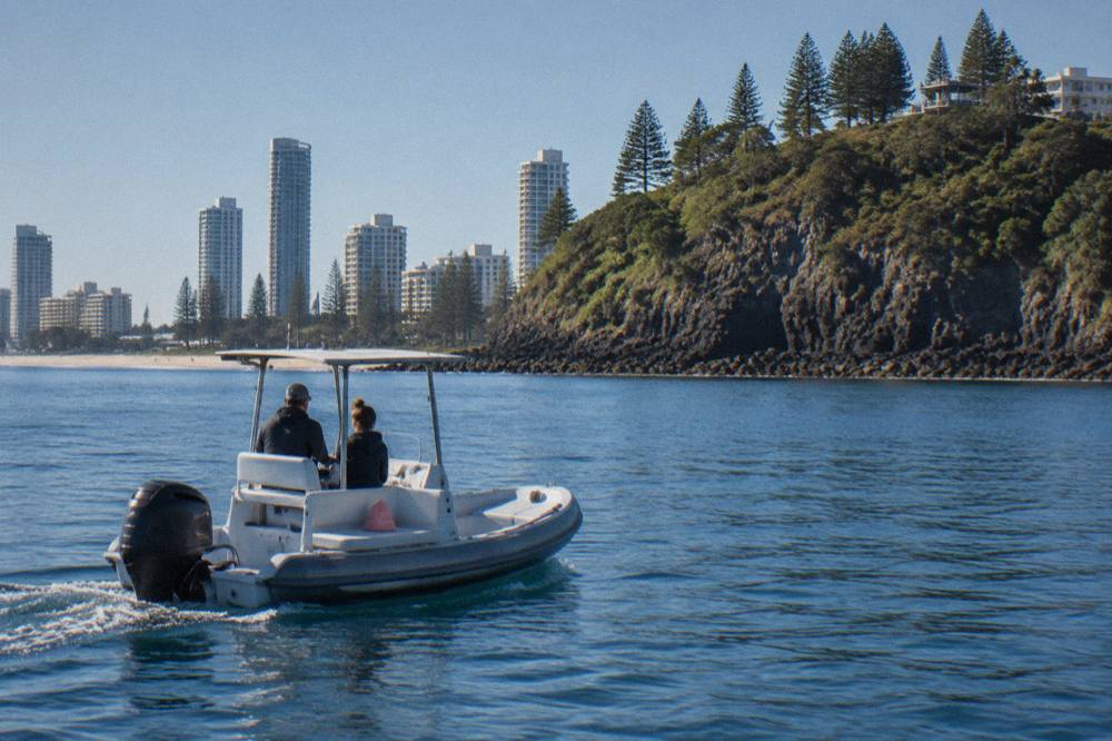 A whale watching boat cruising past a headland on calm blue water