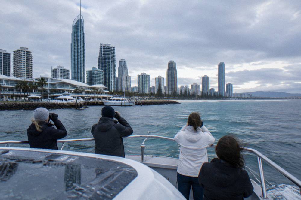 Passengers standing along the bow rail of a whale watching boat scanning open water