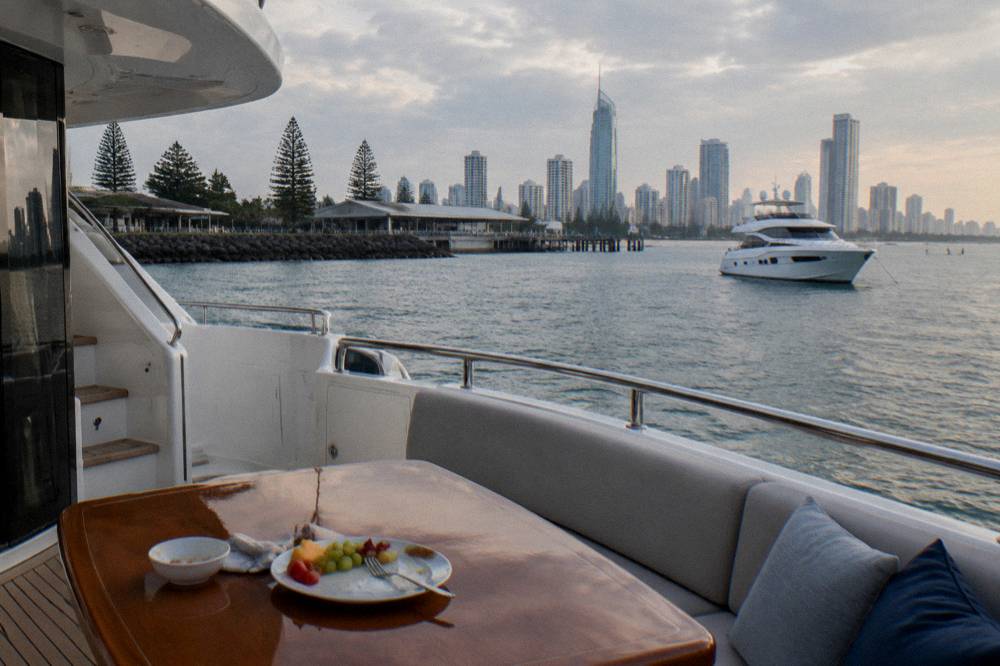 A luxury motor yacht at anchor near a city beachfront skyline