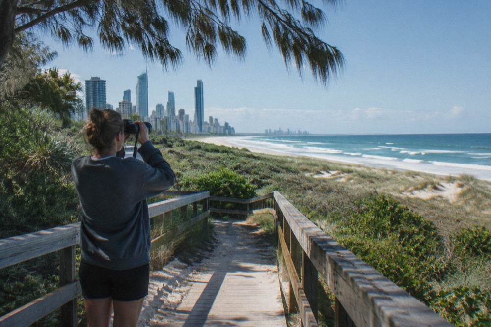 Person with binoculars standing on a grassy headland above open sea