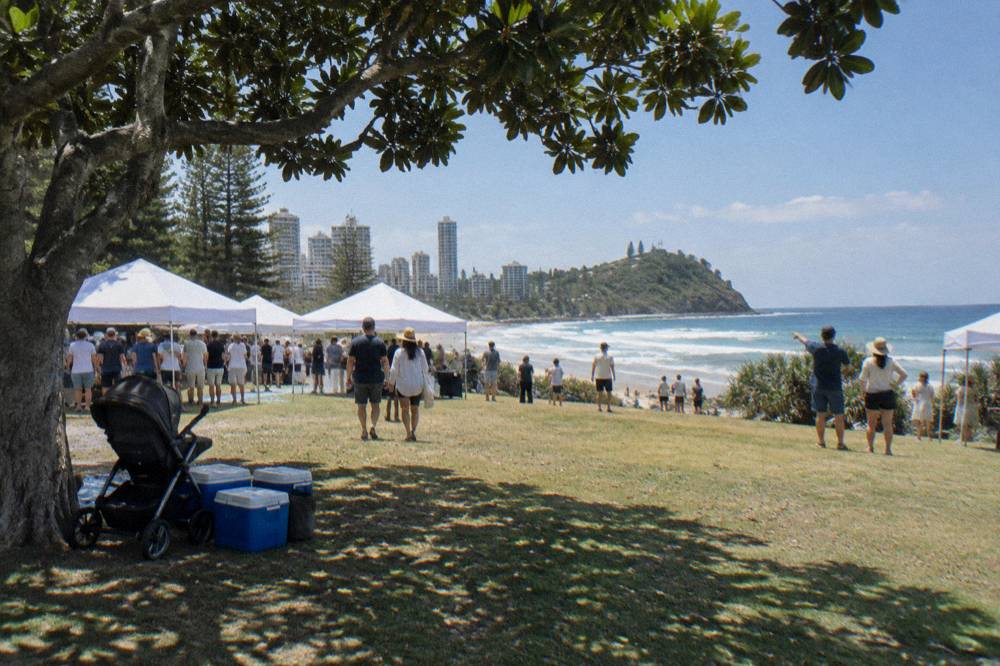 Crowd gathered on a parkland headland beside information stalls near the beach