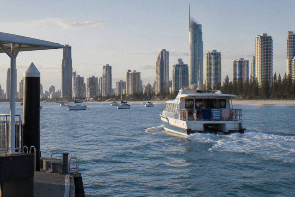 Passenger catamaran cruising past high-rise Gold Coast buildings toward open ocean
