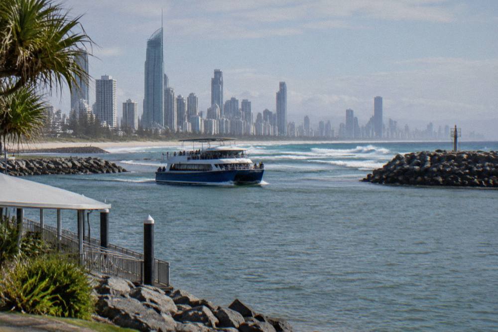 Boats crossing a sandy coastal bar where calm sheltered water meets open ocean swell