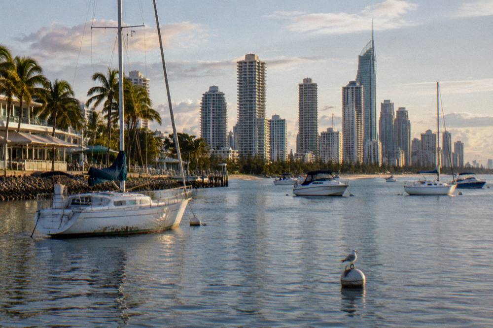 A city skyline of tall towers behind a calm broadwater with boats at anchor
