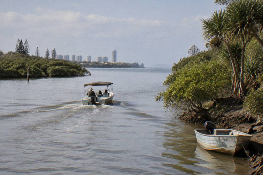 A small safari style boat cruising along a river channel toward open ocean